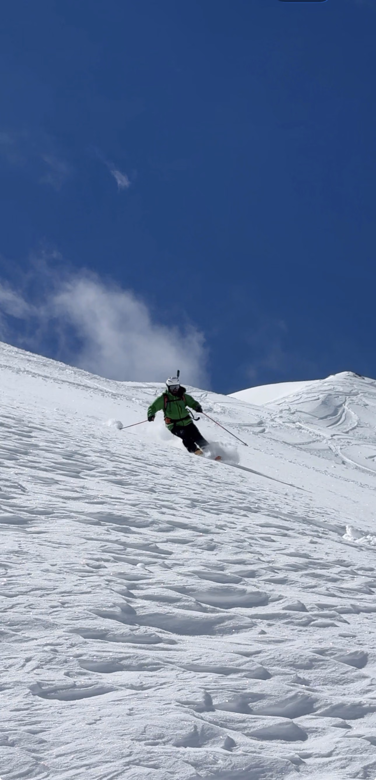 Skier descending a steep mountain couloir under blue sky